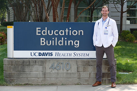 Man in lab coat in front of Education Building sign
