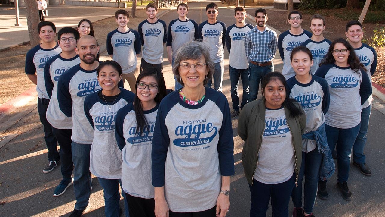 People standing in the formation of a diamond on a street outdoors, all smiling at camera, wearing tshirts that says "First-year Aggie Connections"