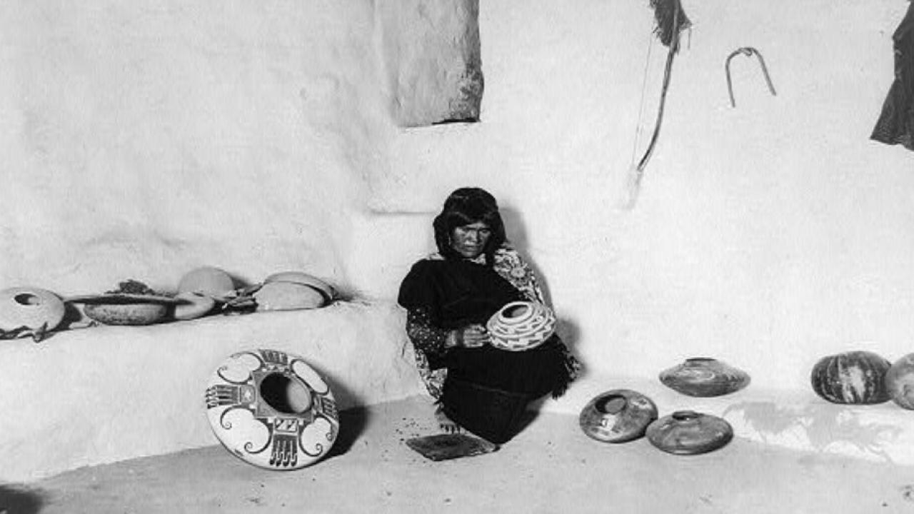 A black and white photo of a a woman decorating pottery 